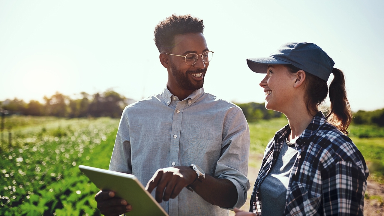 Two people in field. Man holding a clip board.