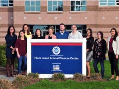 group of people standing behind the sign of the Plum Island Animal Disease Center